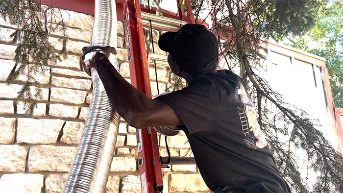 Technician on a ladder handling a long flexible stainless chimney liner against a stone wall